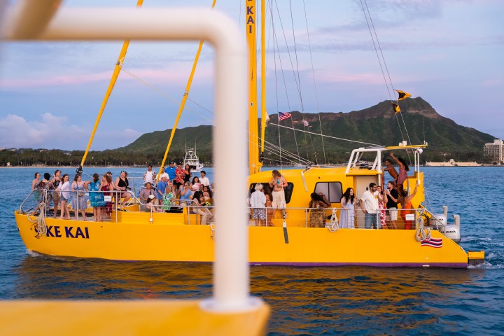 People on a yellow boat in the ocean with a mountain in the background.