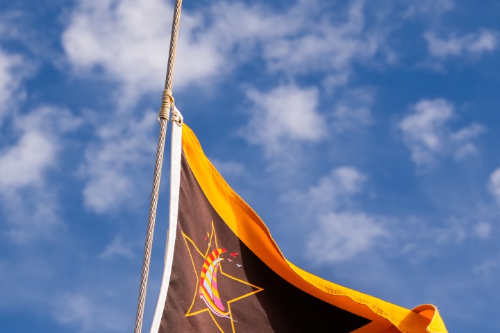 A triangular flag with star design flying against a blue sky with clouds.